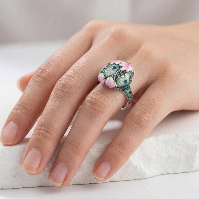Hand wearing a decorative 925 silver lotus enamel ring on a light background