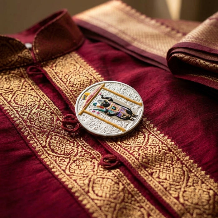 Close-up of a maroon fabric with gold embroidery and a decorative button featuring a Shrinathji 65 grams 999 purity enamel silver coin.