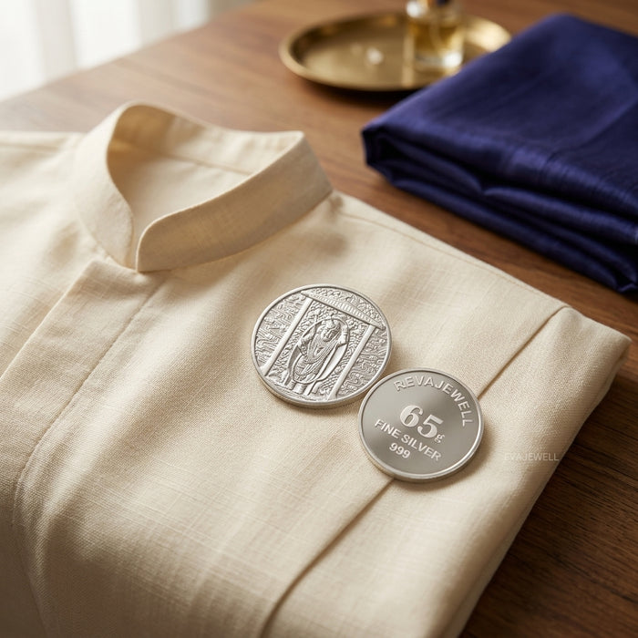 Two Shrinathji 65 grams 999 purity silver coin on a beige fabric surface with a blue cloth and gold object in the background.