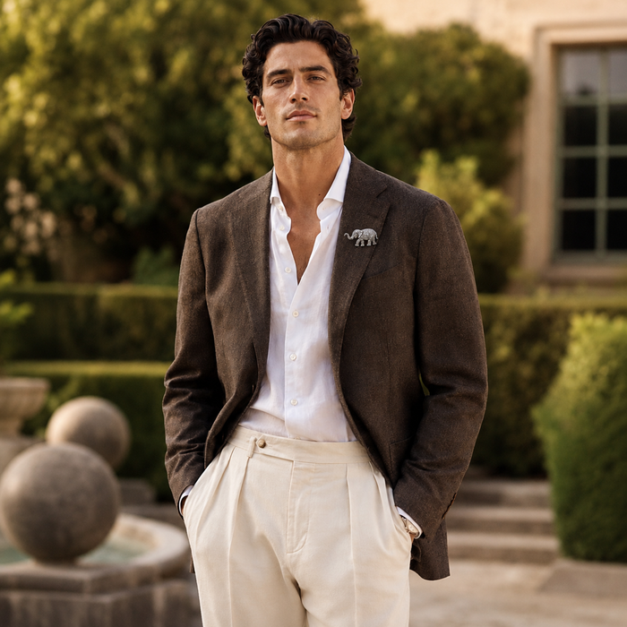 Man in a brown blazer and white shirt outdoors with greenery, wearing a 925 silver elephant moissanite brooch